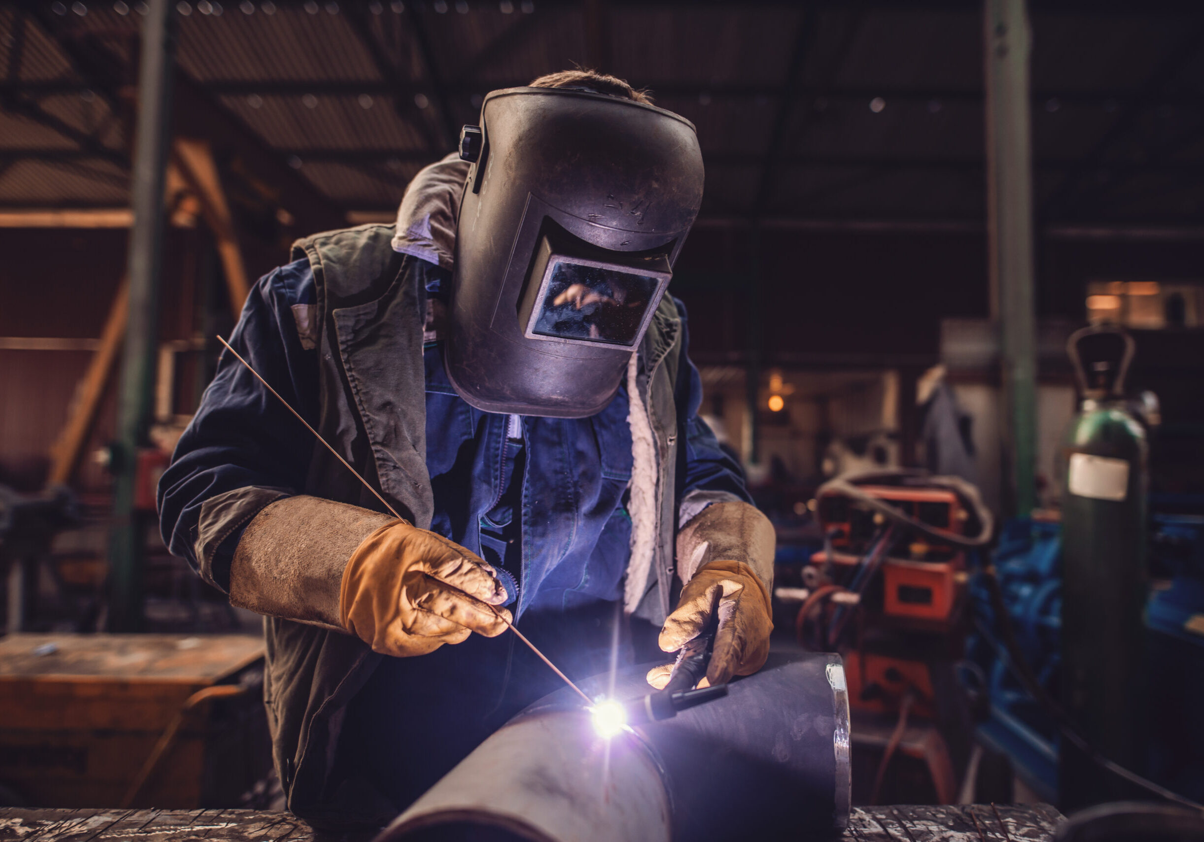Worker welding iron. Protective suit and mask on. Workshop interior. Worker welding iron. Protective suit and mask on. Workshop interior.