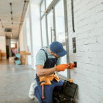 Young man wearing work overalls with    belt while fixing electric wall socket
